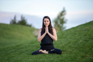 a woman in black leggings meditates on a green meadow